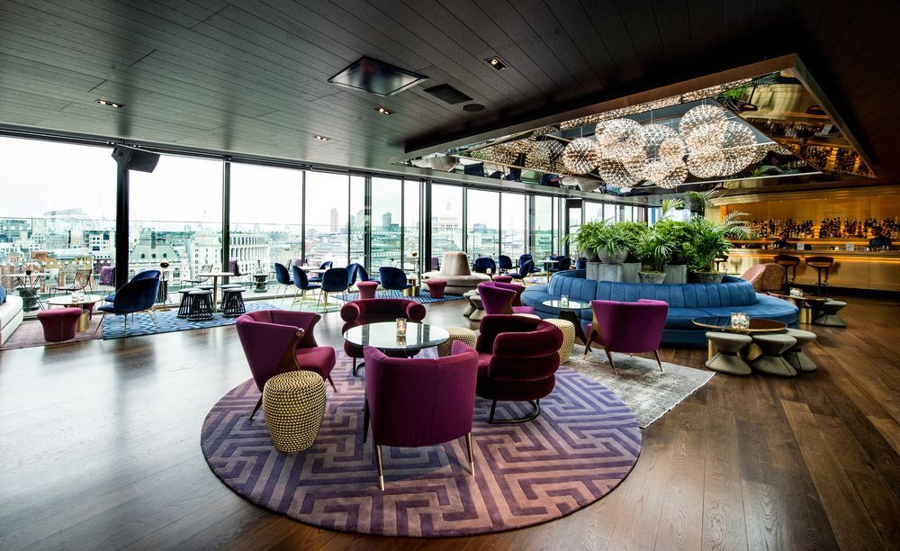 Sea Containers London Hotel Exterior photo The photo shows a stylish and modern interior of a lounge or bar. It features large windows that provide a view of the city, allowing natural light to flood the space. The seating includes plush, purple armchairs arranged around coffee tables on a de